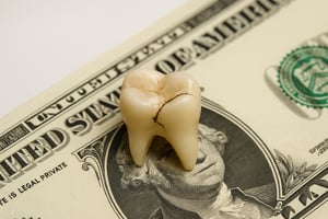 Cracked tooth on money symbolizing the cost of delaying care – Whole Health Solutions Shirley MA Physical Therapy.