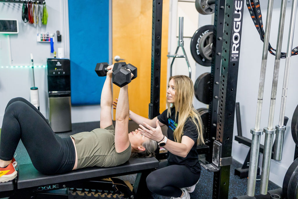 A client performing a strength training exercise with a coach watching closely, emphasizing correct form and muscle engagement.