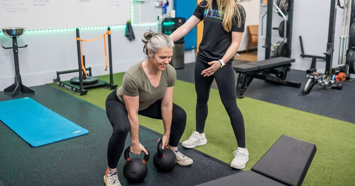 A coach guiding a client through kettlebell deadlifts at Whole Health Solutions in Shirley, MA.